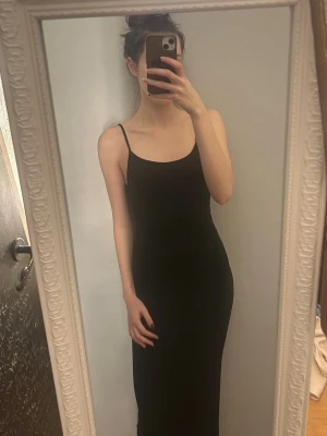 Svart långklänning med öppen rygg - Säljer en svart långklänning med smala axelband och öppen rygg med snörning. Klänningen har en tight passform och är perfekt för dig som vill ha en stilren och elegant look. Materialet känns mjukt och följsamt mot kroppen.