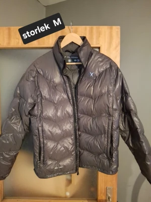 Mörkgrå lättviktsjacka från 2117 of Sweden - Snygg mörkgrå lättviktsjacka från 2117 of Sweden med diskret logga på bröstet. Jackan har dragkedja framtill, hög krage och lätt vaddering som håller värmen. Använd en gång