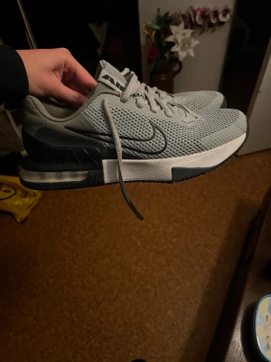 Nike Air Max grå sneakers - Snygga Nike Air Max sneakers i ljusgrå mesh med mörkgrå detaljer och vit sula. Klassisk swoosh på sidan och synlig Air Max-dämpning i hälen. Skorna har snörning och sportig design som passar perfekt till streetwear.