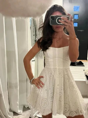 Vit kort klänning med broderad spets - Säljer en vit kort klänning med broderad spets och axelband. Klänningen har en utsvängd kjol och v-ringad överdel. Perfekt för studenten och sommarens alla tillfällen. Materialet är bomull och designen är riktigt söt och feminin. 