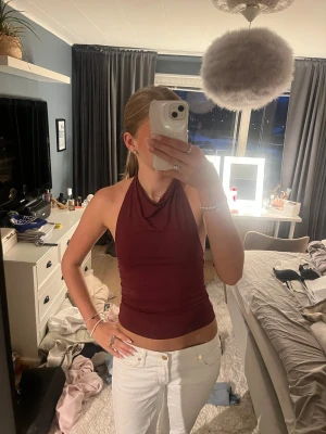 Vinröd halterneck topp - Säljer en vinröd halterneck topp med öppen rygg och croppad passform. Toppen har en snygg drapering framtill och är perfekt för dig som vill ha en trendig och stilren look. Materialet känns mjukt och stretchigt.