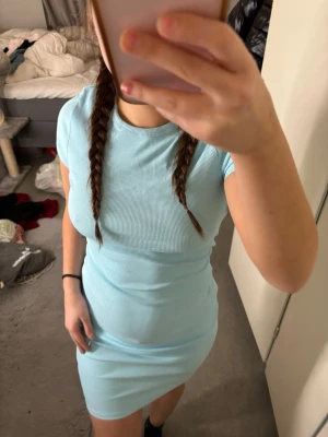 Ljusblå ribbad kortklänning - Säljer en ljusblå ribbad kortklänning med rund hals och korta ärmar. Klänningen har en tight passform och är gjord i ett stretchigt material som sitter snyggt på kroppen. Perfekt för dig som gillar en enkel men stilren look.