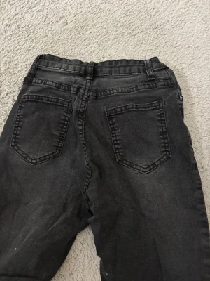 Svarta utsvängda jeans - Säljer ett par svarta jeans med utsvängda ben och klassisk femficksdesign. Jeansen har hällor för skärp och knappstängning framtill. Perfekta för dig som gillar en avslappnad och trendig look.