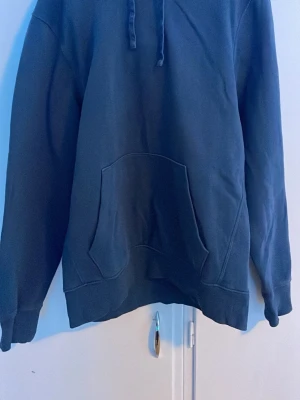 Mörkblå hoodie med magficka - En stilren mörkblå hoodie med klassisk huva och dragsnören. Hoodien har en stor magficka framtill och ribbade muddar vid ärmslut och nederkant. Perfekt för en avslappnad look och enkel att matcha med jeans eller joggers.