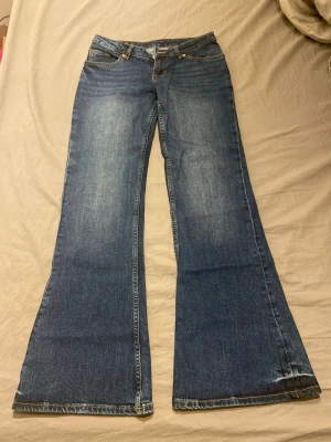 Blå utsvängda jeans från Monki - Säljer ett par blå utsvängda jeans från Monki med snygga broderade gula rosetter på bakfickorna. Aldrig använda! Strl 28 och för korta för mig som är 178!