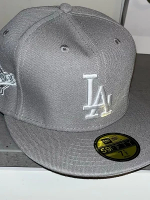 Grå LA Dodgers keps New Era 59FIFTY - Snygg grå keps från New Era 59FIFTY med LA Dodgers-logga broderad framtill i vitt. Klassisk flat peak och broderad MLB-logga baktill. Kepsen är i ett stadigt tygmaterial och har en modern streetwear-look.