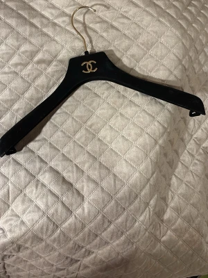 Svart galge från Chanel - Snygg svart galge från Chanel med den ikoniska logotypen i guld på framsidan. Perfekt för att hänga upp dina favoritplagg och ge garderoben en exklusiv touch.