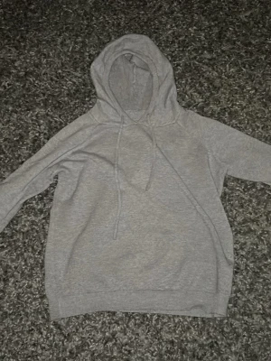Grå basic hoodie med dragsko - Enkel och stilren grå hoodie med huva och dragsko. Hoodien har en avslappnad passform och är tillverkad i mjukt material, perfekt för chill dagar. Inga synliga loggor eller tryck, bara klassisk och clean design.