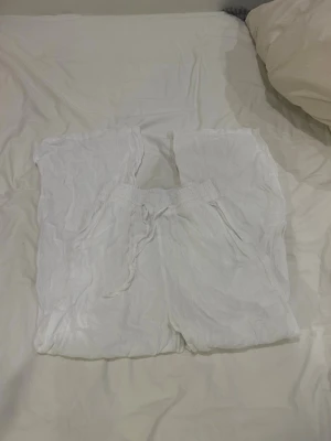 Vita linnebyxor från Gina Tricot - Säljer ett par vita linnebyxor från Gina Tricot med resår och dragsko i midjan. Byxorna har avslappnad passform och sidofickor, perfekta för en chill och luftig stil. Materialet är tunt och svalt linne som passar till sommaren.