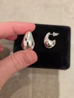 Chunky droppformade silvriga örhängen - Säljer ett par chunky örhängen i droppformad design med blank, silvrig finish. De har en modern och stilren look som verkligen sticker ut. Perfekta för dig som gillar statement-smycken och vill addera lite edge till din outfit.