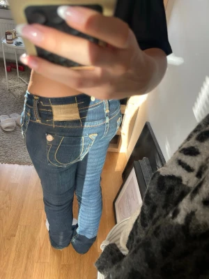 True Religion blå bootcut jeans - Säljer ett par unika mörkblå bootcut jeans från True Religion med ikoniska kontrastsömmar och stora bakfickor med vita detaljer. Jeansen har låg midja. 