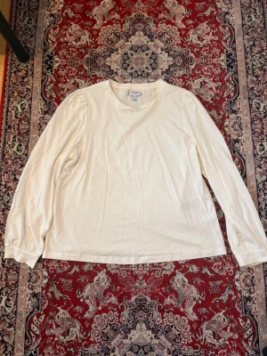 Vit långärmad topp från vero moda  - En enkel och stilren vit långärmad topp från vero moda. Toppen har rund halsringning och är tillverkad i mjuk bomull. Passar perfekt till jeans eller kjol för en clean look. Den är liten i st passar även dig som är L