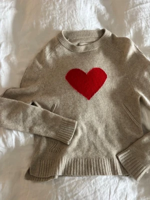 Zadig & Voltaire tröja  - Supersöt beige stickad tröja med ett stort rött hjärta på bröstet. Tröjan har rund halsringning, långa ärmar och ribbade muddar vid ärmslut och nederkant. Perfekt för dig som vill ha en mysig och trendig look. 100% Kashmir 