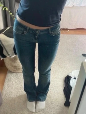 Blå bootcut jeans med låg midja - Säljer ett par klassiska blå bootcut jeans med låg midja och femficksdesign. Jeansen har en snygg passform som framhäver benen och är tillverkade i ett stretchigt denim-material. Perfekta för dig som gillar en klassisk look!