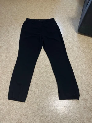 Svarta raka kostymbyxor - Snygga svarta kostymbyxor med rak passform och diskreta fickor. Byxorna har en klassisk look och är perfekta för en stilren outfit. Tillverkade i ett mjukt tyg som ger en skön känsla hela dagen.