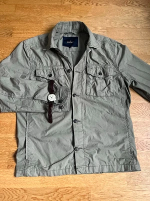 Grön overshirt från Morris Stockholm - Stilren grön overshirt från Morris Stockholm i tunn bomull. Två bröstfickor med knappar, klassisk krage och knappstängning framtill. Perfekt lager på lager-plagg för en avslappnad men snygg look.