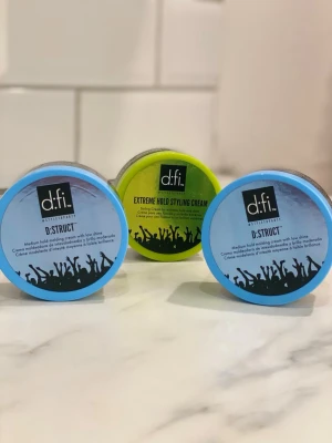 d:fi hårstylingkräm och vax - Tre burkar hårstylingprodukter från d:fi, två blå D:STRUCT medium hold molding cream och en grön Extreme Hold Styling Cream. Produkterna har rund form och lock med svart och färgglad design. Perfekt för att forma och styla håret med olika stadga och glans. Nypris 149 kr styck. Mitt pris 199
