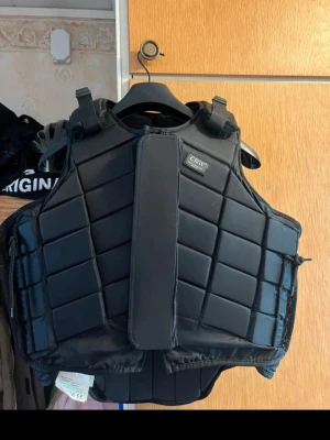 Svart skyddsväst från CRW - Säljer en svart skyddsväst från CRW med quiltad design och justerbara axelband. Västen har dragkedja och kardborrestängning framtill för extra säkerhet och passform. Perfekt för ridning och andra aktiviteter där extra skydd behövs.
