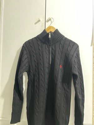 Polo Ralph lauren törja - Snygg  stickad tröja från Ralph Lauren med halv dragkedja och hög krage. Klassisk kabelstickning och röd broderad logga på bröstet. Perfekt för lager-på-lager och en stilren look.