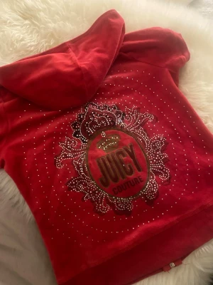 Röd Juicy Couture hoodie vintage - Säljer en vintage röd Juicy Couture hoodie i mjuk velour med korta ärmar och dragkedja. Baksidan har stort glittrigt strassmönster och logga, samt en huva. Pris kan diskuteras 💕M men passar S jätte bra