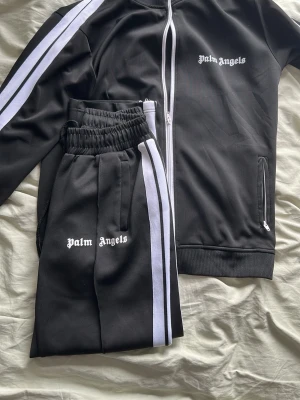Palm Angels svarta mjukisbyxor - Säljer en snygg Palm angels tracksuit då den blivit för liten för mig tyvärr. Dressen är i mycket bra skick med inga defekter. Pris kan diskuteras vid snabb affär :)