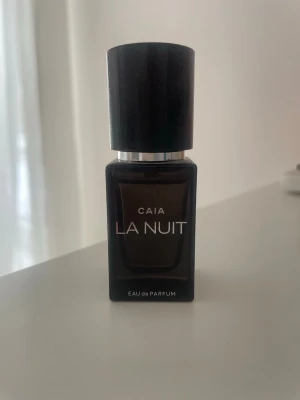 CAIA La Nuit Eau de Parfum 15ml - Säljer en elegant parfym från CAIA, La Nuit Eau de Parfum. Flaskan är mörk och stilren med svart lock och silverdetalj. Rektangulär form och modern design som känns lyxig och trendig. Perfekt för dig som gillar exklusiva dofter.
