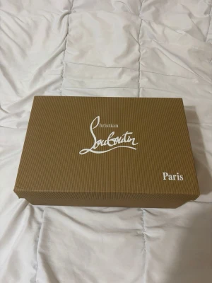 Svarta Louboutin sneakers med nitar - Snygga svarta sneakers från Christian Louboutin med mattsvarta nitar på tån. Skorna har en klassisk låg modell, svarta skosnören och ovandel i mocka. Perfekta för dig som vill sticka ut med en edgy och lyxig stil.