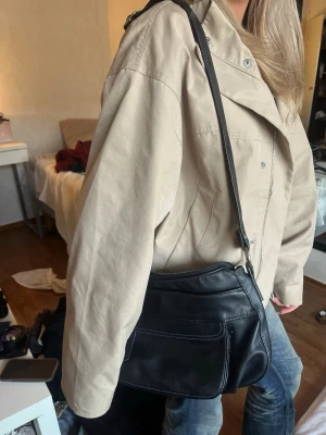 Svart axelväska i skinn - Snygg svart axelväska i mjukt skinn med justerbar axelrem och flera fack framtill