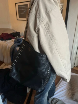 Svart axelväska med nitar - Snygg svart axelväska i mjukt läder med silverfärgade nitar längs kanterna