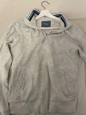 Ljusgrå hoodie från dressman - Ljusgrå hoodie från dressman med dragkedja framtill och två fickor. Tillverkad i mjukt bomullsmaterial och har en klassisk huva. Perfekt för en avslappnad och stilren look.