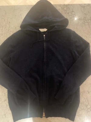 Mörkblå hoodie med dragkedja Sayless - Säljer en mörkblå hoodie från Sayless med dragkedja framtill och justerbar huva. Hoodien har långa ärmar och ribbade muddar vid ärmslut och nederkant. Materialet känns mjukt och passar perfekt för en avslappnad stil. Den övre dragkedjan kan vara lite kronglig 