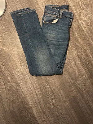Blå raka jeans med klassisk tvätt - Säljer ett par blå jeans med rak passform och klassisk tvätt. Jeansen har fem fickor, bälteshällor och knappgylf. Perfekta till vardagslooken och passar till det mesta. Materialet är troligtvis bomull med lite stretch för extra komfort.