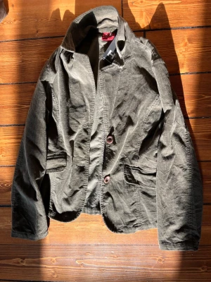 Olivgrön manchesterkavaj - Snygg olivgrön kavaj i manchestertyg i st. Lx men skulle säga att den passar mer M som är köpt på Humanasecondhand . Tvåknäppt modell med breda slag och två framfickor. Perfekt för dig som vill ha en avslappnad men ändå stilren look. Kavajen har en mjuk struktur och klassisk passform.