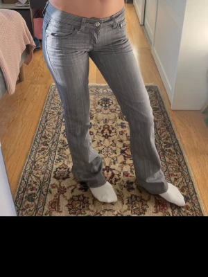 Grå bootcut jeans med låg midja - Snygga grå jeans med bootcut-modell och låg midja. Jeansen har klassiska fem fickor och subtila slitningar för en cool look. Perfekta för dig som gillar en avslappnad men trendig stil.