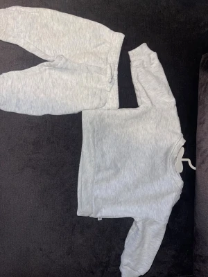 Grått loungewear-set från BEBE - Mysigt tvådelat loungewear-set från BEBE i ljusgrått. Setet består av en långärmad tröja med tryckknappar vid axeln och matchande byxor med resår i midjan. Perfekt för bebisar 2-4 månader. Tillverkat i mjukt och bekvämt material.