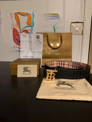 Burberry  bälte - Säljer ett ikoniskt Burberry bälte med klassiskt beige och brunt rutigt mönster samt ett stort guldfärgat B-spänne. Bältet har exklusiv känsla och levereras med originalpåse, box.
