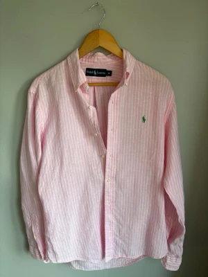 Rosa randig skjorta från Ralph Lauren - Säljer en unik rosa linneskjorta från Ralph Lauren med vita ränder och broderad grön logga på bröstet. Perfekt till sommaren som man kan ha över en t shirt eller liknande. Skick: 10/10 storlek: M                                            Hör av er vid minsta fundering!                                                //Ville