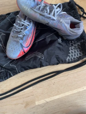 Nike Mercurial fotbollsskor blå/röd - Säljer ett par Nike Mercurial fotbollsskor elite blått med röda och svarta detaljer. Skorna har låg profil, snörning och genomskinlig sula med dobbar för bra grepp på planen. Ovandelen är i syntetmaterial och designen är riktigt sportig och modern. Väl använda men är fortfarande i bra skick