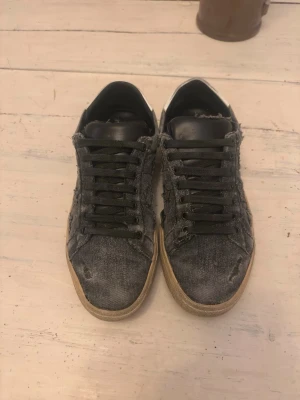 Saint Laurent sl/06 - Jävligt feta vintage distressed Saint Laurent sneakers i en extremt unik och fet colourway. Fina slitningar och fades i materialet som givetvis är fabrikat. De är grå/svarta med typ jeansmaterial och ett riktigt fett stjärnmöster samt en tunga av läder. De är i ganska fint skick och självklart äkta, storlek 43,5. Bara hör av dig vid intresse eller funderingar! 