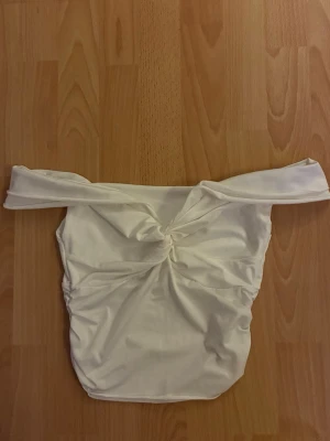 Vit off-shoulder topp - Stilren vit topp med off-shoulder design och twistad detalj framtill. Toppen är axelbandslös och har en smickrande passform med stretchigt material som känns bekvämt mot huden. 