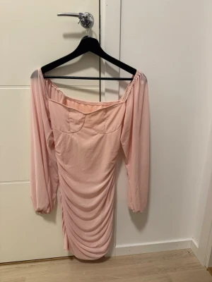 Ljusrosa offshoulder klänning Shein - Trendig ljusrosa kortklänning från Shein med offshoulder-design och långa ärmar. Klänningen har snygg rynkning framtill och en figurnära passform som framhäver siluetten. Tillverkad i mjukt syntetmaterial, perfekt för dig som gillar en feminin och modern stil.