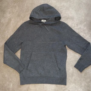 Mörkgrå hoodie från COS - Snygg mörkgrå hoodie från COS med klassisk huva och dragsko. Tillverkad i mjukt stickat material och har en stor magficka framtill. Perfekt för en chill och stilren look. Personen på bilden är 180 och väger 72