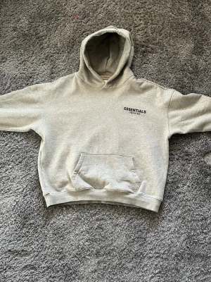 Essentials Fear of God hoodie – beige – size S (passar M) - Säljer en hoodie från Essentials Fear of God. Tvättad endast en gång så den är i nästan helt nytt skick. Inga fläckar eller skador.  Storlek S men modellen är oversized så den passar mer som en M,  Storlek S passar också bra för dom som vill lite oversized. Väldigt skön och populär hoodie.