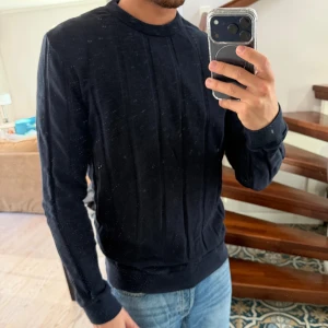 Mörkblå stickad tröja från H&M - Snygg mörkblå stickad tröja från H&M med rund halsringning och diskreta vertikala ränder i stickningen. Tröjan har långa ärmar och ribbade muddar vid ärmslut och nederkant. Perfekt till jeans för en clean och enkel look.