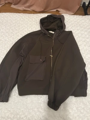 Brun grön hoodie med fickor och huva - Snygg brun grön hoodie/ zipper med fickor framtill och justerbar huva med dragsko. Hoodien har resår vid ärmsluten och en avslappnad passform. Materialet känns mjukt och bekvämt mot huden. Storlek S men passar även som M. 