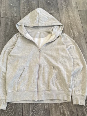 Grå zip-hoodie - En enkel och stilren grå zip hoodie i bra kvalitet. Hoodien har en klassisk huva och ribbade muddar vid ärmslut och nederkant. Perfekt för en avslappnad look. Materialet är en mjuk och bekväm bomullsblandning  med 95% bomull. Jag är 190cm lång, väger 90 och tröjan sitter okej, men är lite kort. Mått på tröjan är: Axelbredd: 49cm Längd:65cm Ärmlängd:64cm