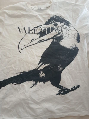 Vit Valentino t-shirt med fågeltryck - Vit t-shirt från Valentino med ett stort svart tryck av en fågel på framsidan. T-shirten har klassisk passform och rund halsringning. Med en oversized passform.