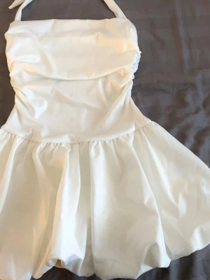 Vit kort klänning med knytband - Vit kort klänning med volangkjol och knytband i nacken. Perfekt för studenten. 