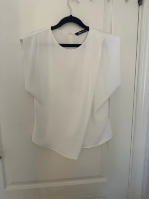 chic vit blus från Zara - Stilren vit blus från Zara med asymmetrisk design och rund halsringning. Blusen är aldrig använd. Den har även en dragkedja vid sidan. Hör av er vid funderingar!💗