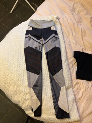 Mönstrade träningstights i grått och svart - Snygga träningstights med grafiskt mönster i olika nyanser av grått, svart och vitt. Hög midja och åtsittande passform, perfekta för gymmet eller löpning. Materialet är stretchigt och följsamt för maximal rörelsefrihet. Uppskattning storlek xs